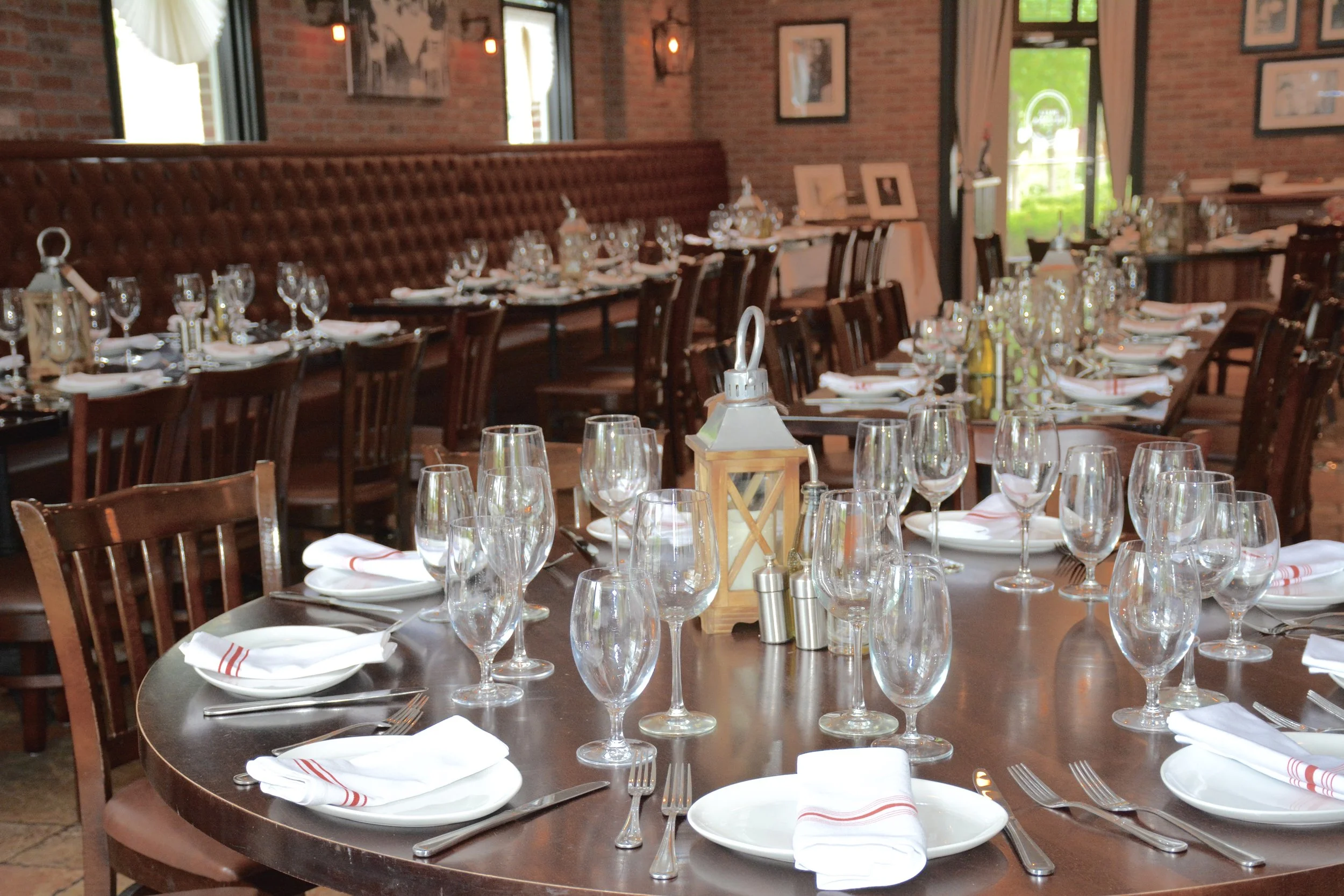 Elegant restaurant dining room with brick walls, leather booth seating, round tables set with glassware and candles